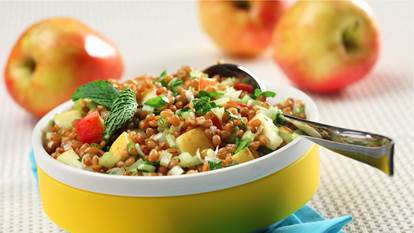 Wheat berry and apple salad in a yellow bowl on a blue napkin.